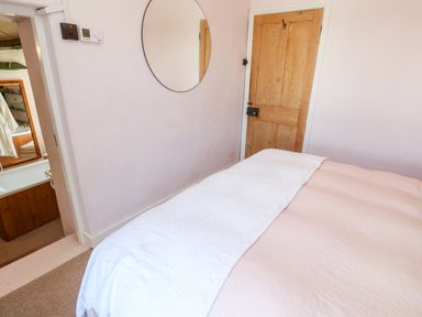 A bedroom with a bed covered in pink and white blankets a wooden door a circular wall mirror and a bathroom visible through an open doorway at Pentira in Kuggar