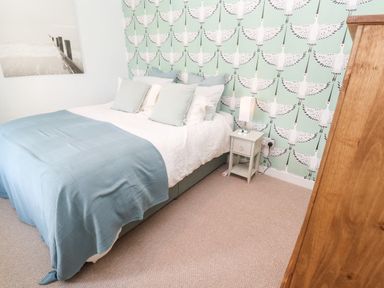A bedroom with a bed with blue blanket and pillows a nightstand with a lamp a wooden wardrobe and patterned wallpaper at Pentira in Kuggar