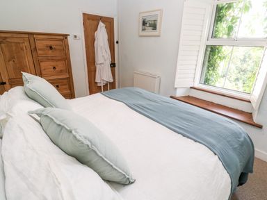 A bedroom with a bed with white and blue bedding a wooden wardrobe a wooden door with white robes hanging and a window with white shutters at Pentira in Kuggar