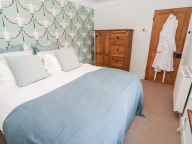A bedroom with a bed covered with blue and white bedding and pillows a wooden cabinet a wooden door with white robes hanging and a radiator at Pentira in Kuggar
