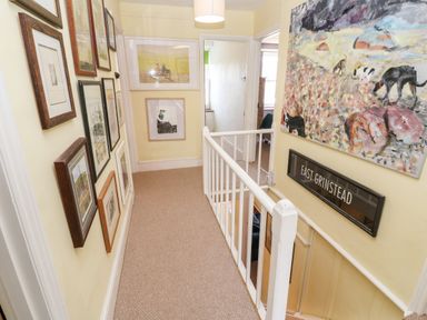 A hallway with framed pictures on walls carpeted floor and a white railing at Pentira in Kuggar