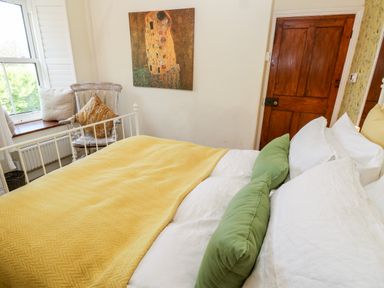 A bedroom with a bed covered in yellow and white bedding with green pillows a wooden door a chair with cushions and a window at Pentira in Kuggar