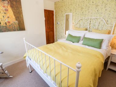 A bedroom with a white metal bed frame yellow bedding green and yellow pillows floral wallpaper and a wooden door at Pentira in Kuggar