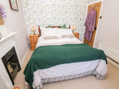 A bedroom with a double bed green blanket floral wallpaper bedside tables and lamps at Pentira in Kuggar