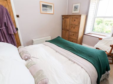 A bedroom with a bed covered in white bedding and a green blanket with a wooden wardrobe and framed pictures on the wall at Pentira in Kuggar