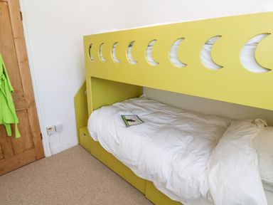 A bedroom with a yellow bunk bed with crescent moon cutouts and a wooden door with a green towel hanging