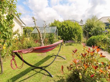 A garden with a striped hammock on a metal frame and a greenhouse in the background at Pentira in Kuggar