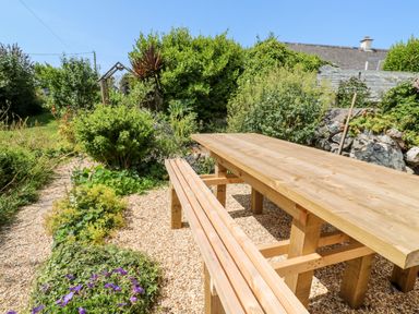 A wooden picnic table with benches in a garden with gravel and various plants and bushes at Pentira in Kuggar