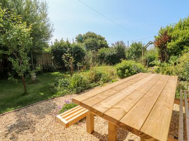 A wooden picnic table on a gravel area next to a garden with grass bushes and trees at Pentira in Kuggar