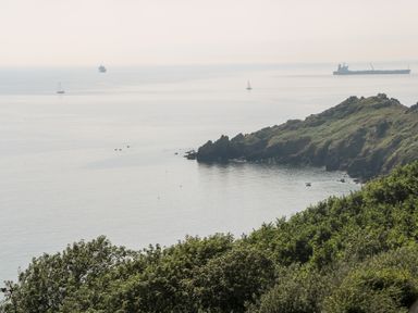 A coastal view with a rocky headland and ships on calm water at Pentira in Kuggar