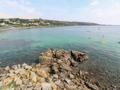 A rocky coastline with clear water and people kayaking near a bay with houses and hills in the background at Pentira in Kuggar