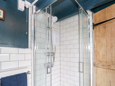 A bathroom with a glass shower enclosure white tiled walls a wooden door and a blue towel on a radiator at Pentira in Kuggar