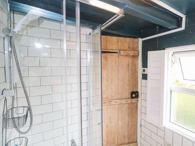 A bathroom shower with white tiled walls a wooden door and a window with shutters at Pentira in Kuggar