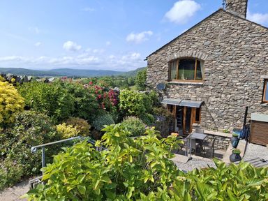 A garden with a stone house and seating area at Horse and Farrier Barn in Newton in Cartmel near Cartmel