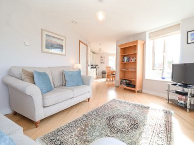 A living room with two beige sofas a wooden bookshelf a television on a stand and a dining area at 23 Tibbys Way in Southwold