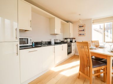 A kitchen with white cabinets black countertops and a wooden dining table with chairs at 23 Tibby's Way in Southwold