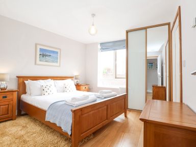 A bedroom with a wooden bed and side tables a window and a wardrobe with mirrored sliding doors at 23 Tibbys Way Southwold