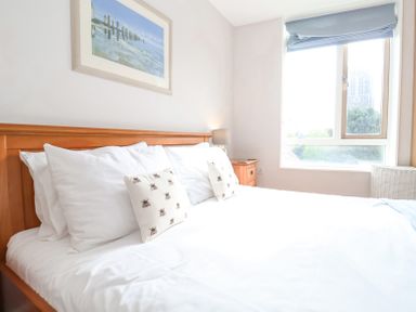A bedroom with a wooden bed frame white pillows and a window with a blue blind at 23 Tibby's Way Southwold