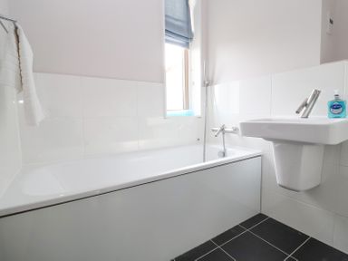 A bathroom with a bathtub a sink a towel on a rack and a bottle of soap on the sink at 23 Tibby's Way in Southwold