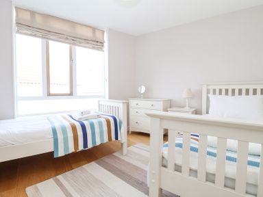 A bedroom with two single beds with striped blankets a dresser with a mirror a bedside table with a lamp and a window at 23 Tibby's Way in Southwold