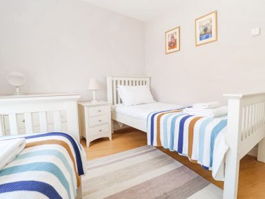 A bedroom with two single beds covered with striped blankets a bedside table with a lamp and a dresser with a mirror at 23 Tibbys Way in Southwold