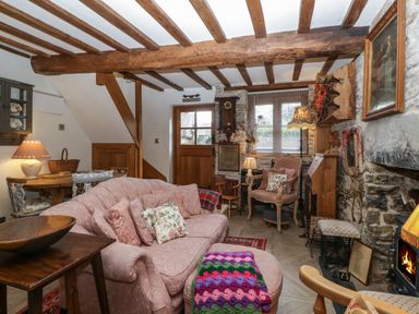 A living room with wooden beams stone walls a pink sofa a fireplace and wooden furniture at Hoarders Cottage in Hay-On-Wye