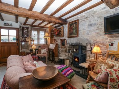 A living room with exposed wooden beams stone walls wood burning stove and various chairs at Hoarders Cottage in Hay-On-Wye