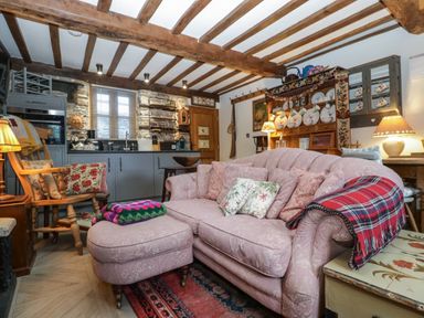 A living room with a pink sofa and ottoman a wooden rocking chair and kitchen cabinets at Hoarders Cottage in Hay-On-Wye
