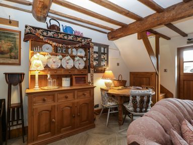 A dining area with wooden furniture and beams with plates and cups on a cabinet at Hoarders Cottage in Hay-On-Wye