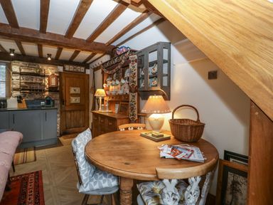 A dining area with a round wooden table and chairs under a wooden beam ceiling at Hoarders Cottage in Hay-On-Wye