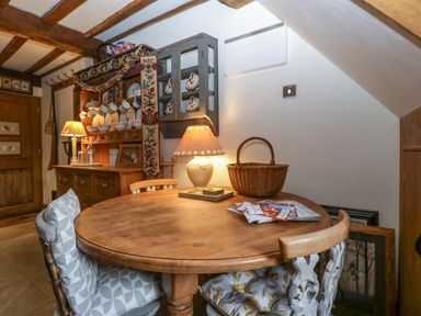 A wooden round table with chairs and a basket in a dining area with wooden beams and cabinets at Hoarders Cottage in Hay-On-Wye