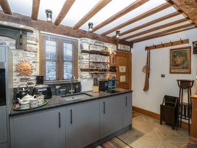 A kitchen with countertop sink toaster kettle and wall shelves with glasses at Hoarders Cottage in Hay-On-Wye