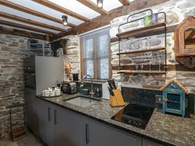 A kitchen with a stone wall and wooden beams featuring a countertop with a sink toaster knife block and an electric stove at Hoarders Cottage in Hay-On-Wye
