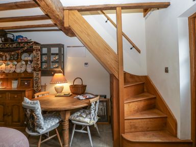 A wooden staircase next to a round wooden table with two chairs and a lamp in a dining area at Hoarders Cottage in Hay-On-Wye