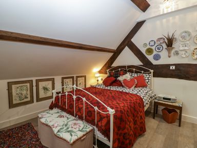 A bedroom with a white metal bed frame a red blanket floral pillows and decorative plates on the wall at Hoarders Cottage in Hay-On-Wye