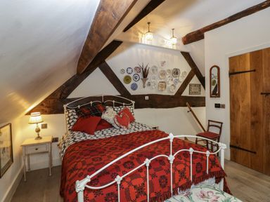 A bedroom with a white metal bed frame red and patterned bedding wooden beams on the ceiling and decorative plates on the wall at Hoarders Cottage in Hay-On-Wye