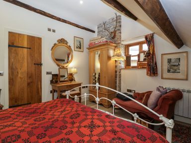 A bedroom with a wooden wardrobe dressing table and a red patterned bedspread at Hoarders Cottage in Hay-On-Wye