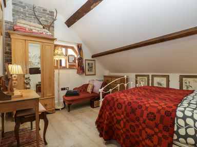 A bedroom with a wooden wardrobe a red chaise lounge a bed with a red blanket and wooden beams on ceiling at Hoarders Cottage in Hay-On-Wye