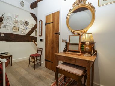 A room with a wooden door a dressing table with mirrors a lamp and a chair with decorative plates on the wall at Hoarders Cottage in Hay-On-Wye