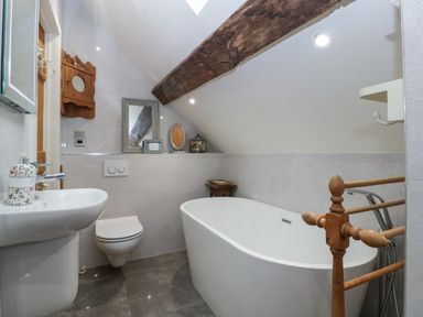 A bathroom with a bathtub toilet sink mirror and wooden beam at Hoarders Cottage in Hay-On-Wye