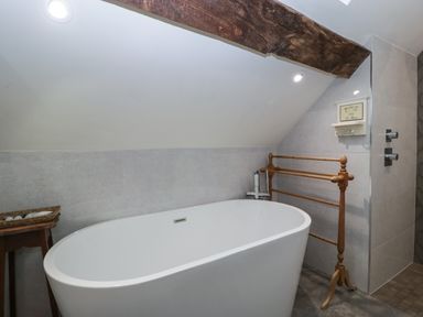 A bathroom with a freestanding bathtub a wooden towel rack and a small table with a basket at Hoarders Cottage in Hay-On-Wye