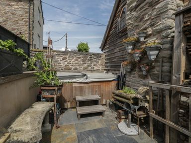 An outdoor patio area with a covered hot tub wooden steps stone bench and planters on stone walls at Hoarders Cottage in Hay-On-Wye