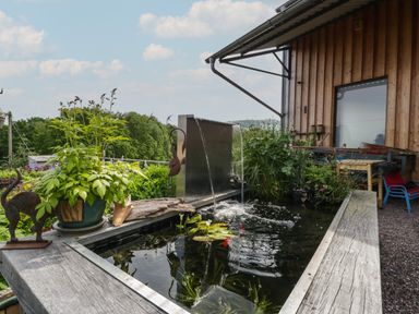 An outdoor water feature with plants and a metal waterfall near a wooden building at Hoarders Cottage in Hay-On-Wye