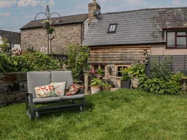 A garden with a grey outdoor bench with cushions a lawn and plants in pots at Hoarders Cottage in Hay-On-Wye