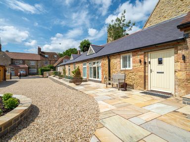 Exterior view of a stone house with a paved patio bench and gravel driveway at The Stables in Wheatley