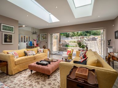 A living room with yellow sofas and a pink ottoman opening to an outdoor stone patio at The Stables in Wheatley