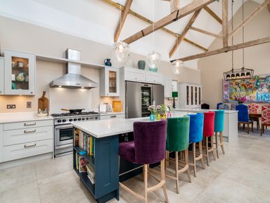A kitchen with a large island and colorful bar stools under wooden beams at The Stables in Wheatley