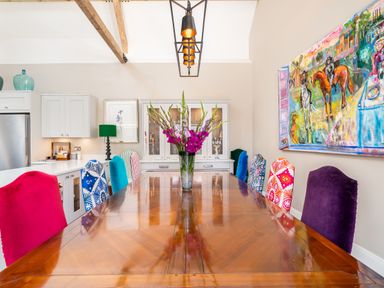 A dining room with a long wooden table surrounded by colorful chairs and a vase with flowers on the table at The Stables in Wheatley