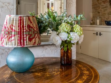 A table with a blue lamp with a patterned shade and a brown vase with flowers in a room at The Stables in Wheatley