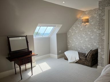 A room with a wooden vanity table with mirror near a window and a patterned sofa with a white blanket at The Stables in Wheatley